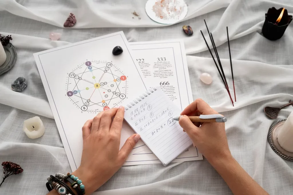Imagem de uma mesa com elementos de numerologia cabalística, cadernos com cálculos numéricos e cristais, representando o estudo dos números pessoais e espirituais.
