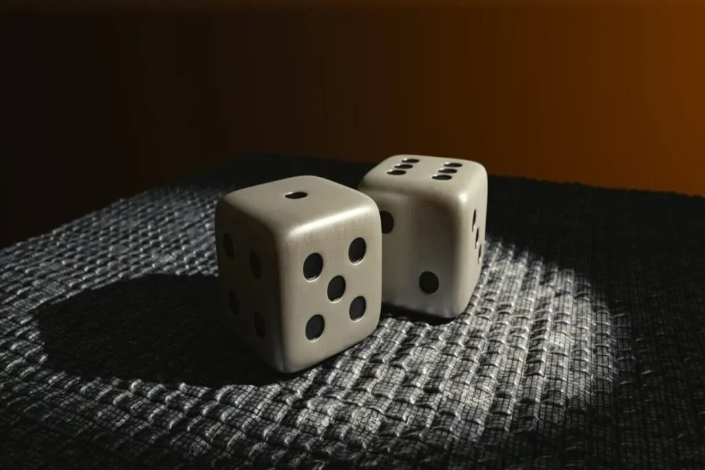 Dois dados cinza com faces numeradas consecutivamente em destaque sob luz natural sobre superfície escura