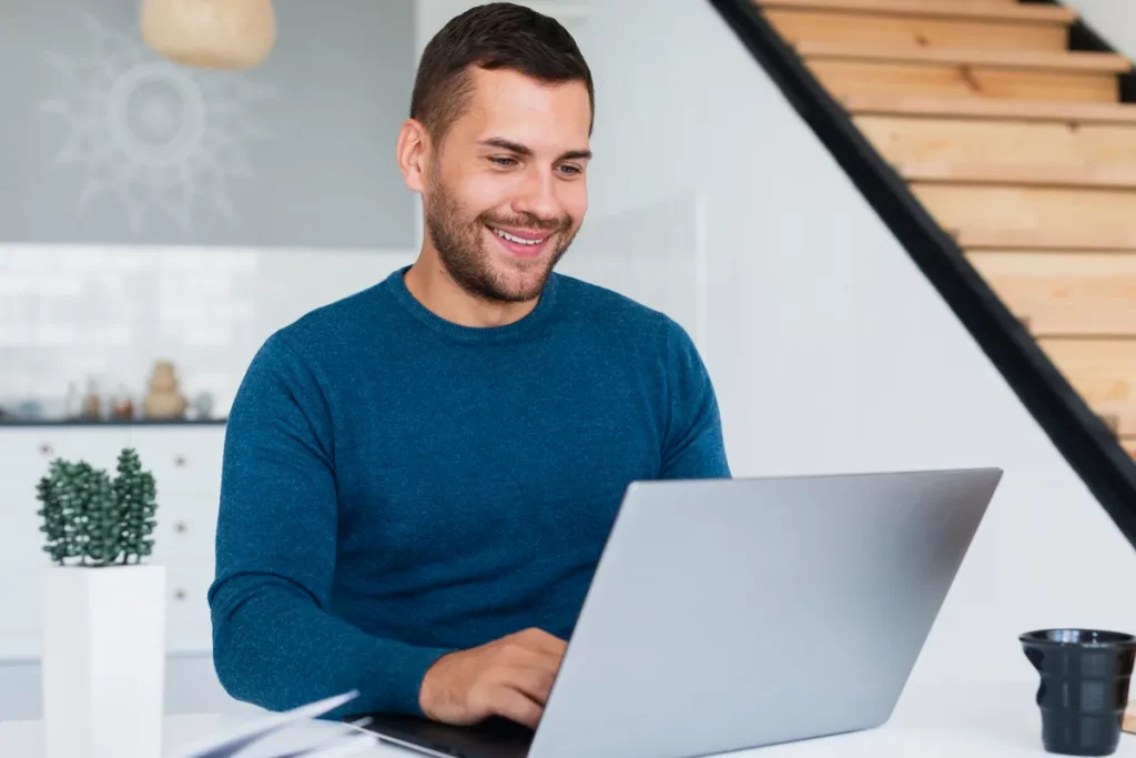 Homem sorridente usando notebook em ambiente moderno e iluminado.