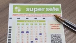 Volante da loteria Super Sete parcialmente preenchido com caneta, sobre mesa de madeira.