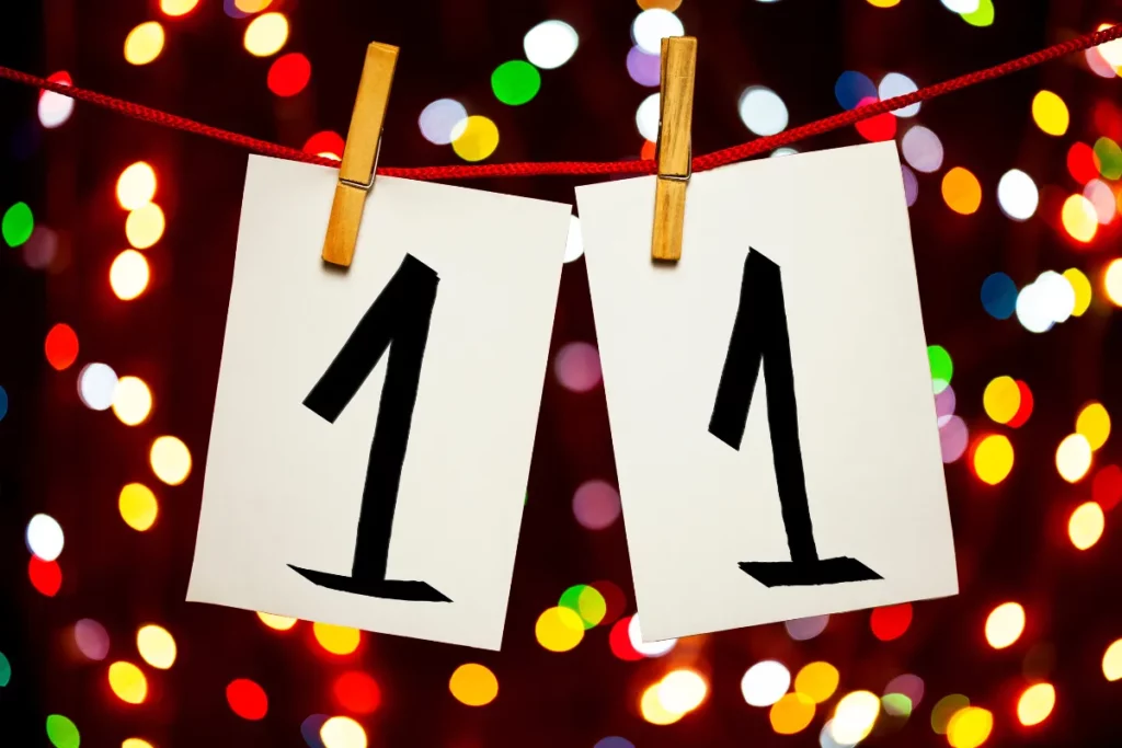 dois cartoes com o numero 1 pendurados em um barbante formando o numero 11 com luzes coloridas ao fundo