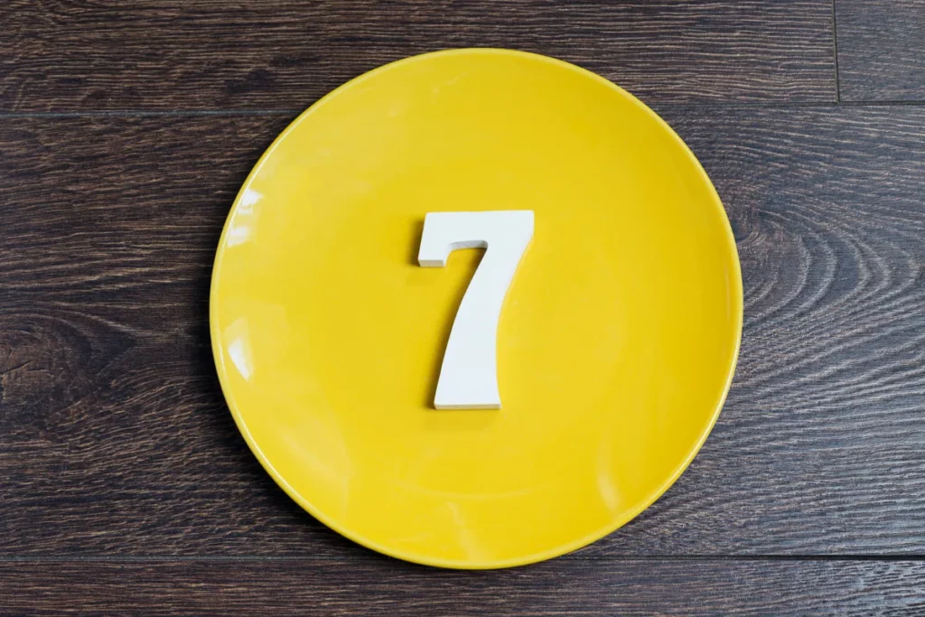 número 7 branco colocado sobre um prato amarelo em superfície de madeira